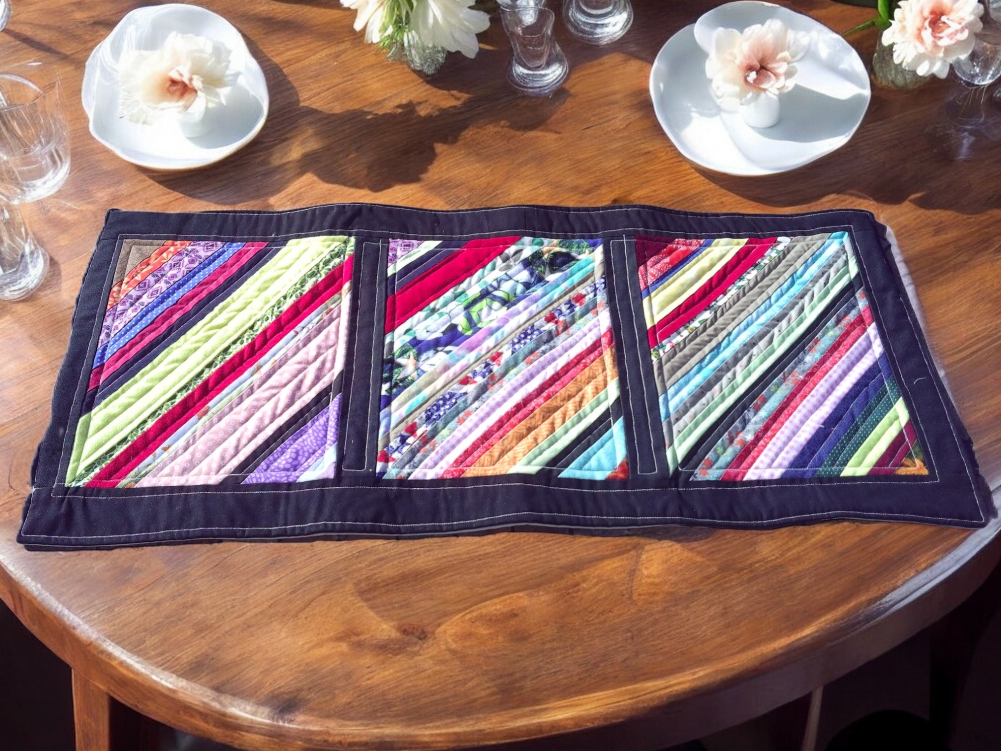 Colorful scrappy quilted table runner with navy border on a wooden table, handmade by Reading Well Handmade